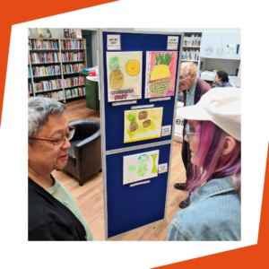 Photo showing 2 people looking at Richmond AID's art exhibition at Teddington Library